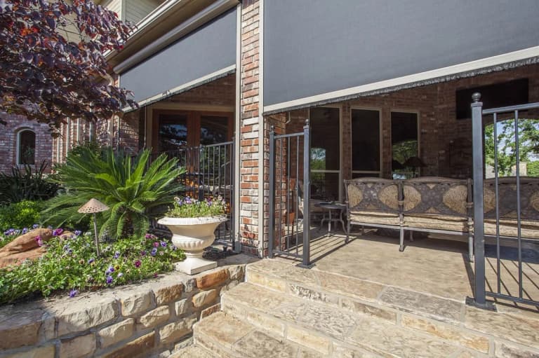 Motorized screens partly lowered across a brick covered patio with outdoor seating