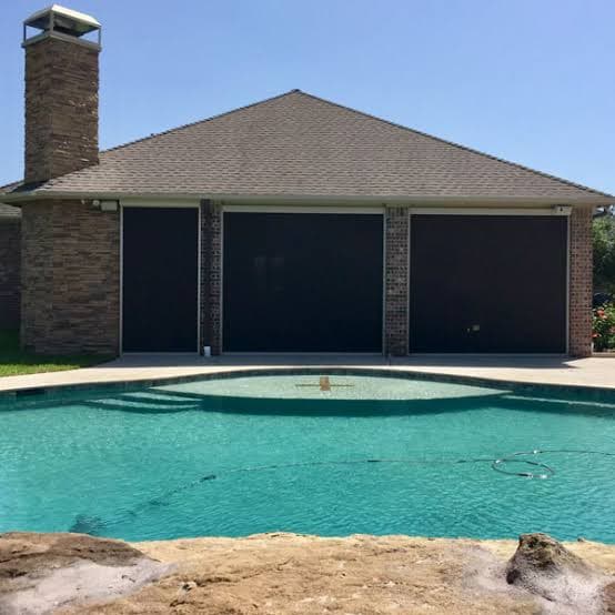 Three dark retractable screens closing in a pool house patio across from a swimming pool